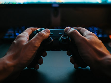 Руки держат игровой контроллер в тёмной комнате с подсветкой монитора — погружение в видеоигры